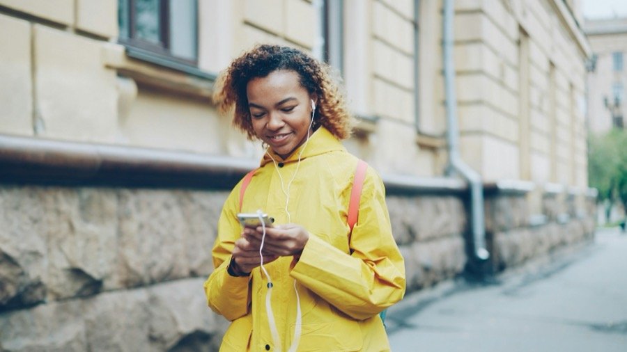 Jeune femme en manteau jaune, téléphone en main, dans une rue de Montpellier